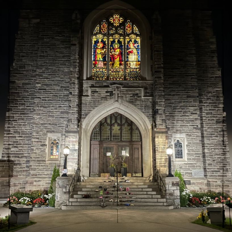 Rows of children's shoes on the front steps of a stone church at night, its doors closed